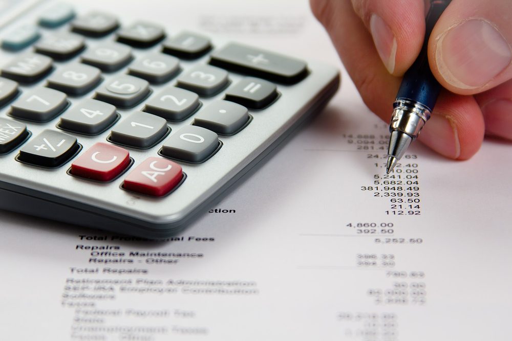 A hand checking figures on a printed financial statement with a calculator